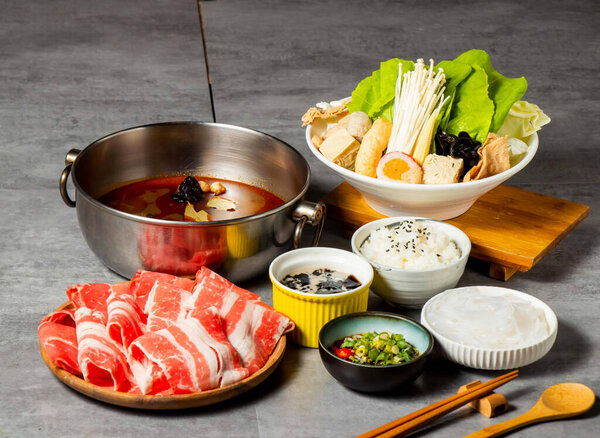 Red Fire Spicy Double Hot Pot Set with Sliced Meat, Vegetables, rice, noodles, mushroom and Dipping Sauces isolated on background side view of taiwan food
