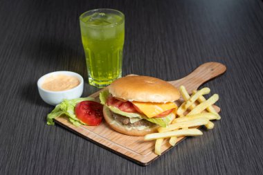 Klasik sığır burger yemeği, patates kızartması, mayonez sosu ve ahşap masa başı Amerikan yemeği manzaralı soda.