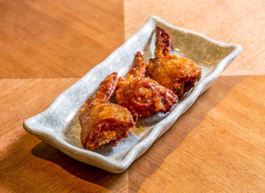 Kızarmış tavuk kanatları, ana yemek olarak ahşap tahta tarafında dikdörtgen tabakta tuzlu pilav ile doldurulmuş.