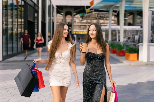 年轻的女性购物狂们穿着时髦的衣服 头戴彩色纸袋和咖啡 周末在城市街道上购物时互相微笑 互相交谈 — 图库照片