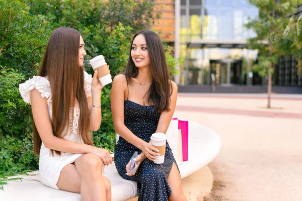 Современные Молодые Женщины Модных Платьях Отдыхают Скамейке Кофейными Чашками Вынос — стоковое фото