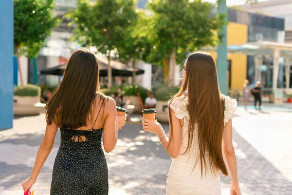 在城市阳光明亮的街道上购物后 穿着纸杯咖啡去散步的年轻女友们的背影 — 图库照片