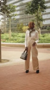 Kendine güveni tam bir kadın şık giyinmiş ve geleneksel İslami başörtüsü boynunda atkıyla parkta dikilip başka tarafa bakıyor.