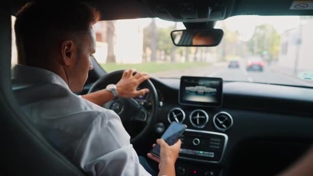 Seorang Pria Berbaju Putih Menggulir Berita Ponsel Ketika Mengendarai Mobil — Stok Video