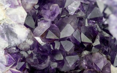 Keskin ve canlı mor ametist kristal kümelerini doğal geometrik yüzeylerle gösteren detaylı makro yakın çekim fotoğrafı