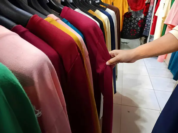 a woman is choosing clothes shop looking through a clothes hanger with different casual colorful clothes on a clothes hanger, clothes shopping concept.