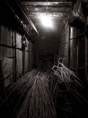  Görüntü loş bir oda yakalıyor, muhtemelen bir bodrum, büyük saman benzeri nesnelerle dolu..