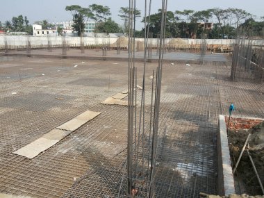 31 Temmuz 2024 Dhaka, Bangladeş. Görüntü, yerde metal kirişler ve ahşap kalaslarla tamamlanmamış bir inşaat alanını gösteriyor..