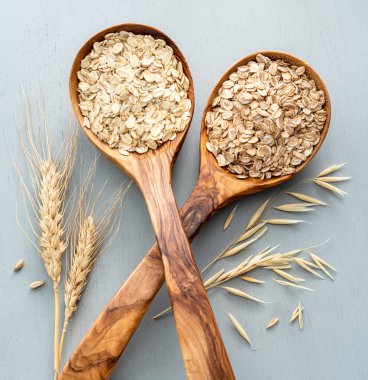 Yulaf ve buğday gevrekleri gri arka planda tahta kaşıklarda. Sağlıklı konsept.