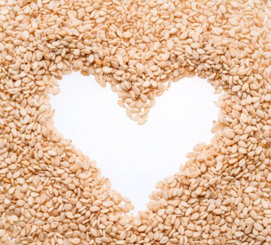 White sesame seeds arranged in shape of heart isolated on white background. Top view.