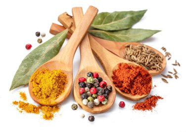 Beyaz arka planda otlar ve baharatlarla çevrili ahşap kaşıklarda farklı renkte baharatlar..