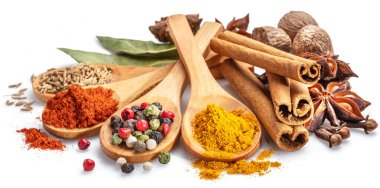 Beyaz arka planda otlar ve baharatlarla çevrili ahşap kaşıklarda farklı renkte baharatlar..