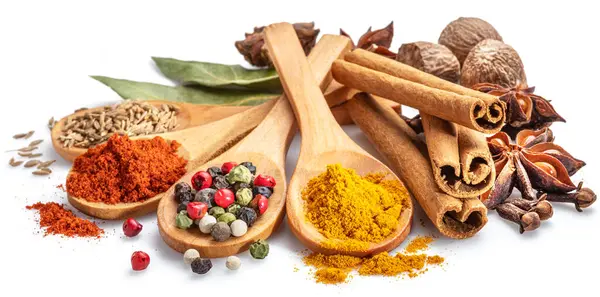 Beyaz arka planda otlar ve baharatlarla çevrili ahşap kaşıklarda farklı renkte baharatlar..