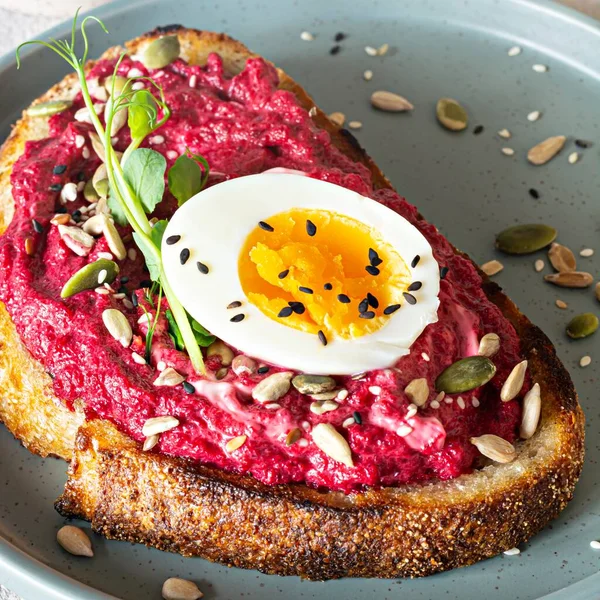 Whole grain toast with beetroot hummus, seeds, egg and microgreens (sprouted pea sprouts) on a light gray background. The concept of healthy eating..