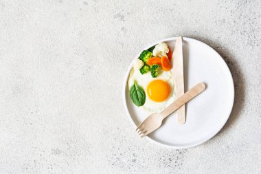 Healthy breakfast of fried egg and boiled vegetables with spinach on a light background. Healthy food concept, minimalism, top view.