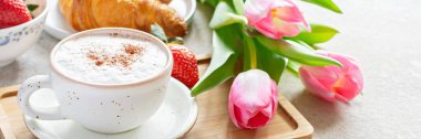 Happy mother's day, beautiful breakfast, lunch with cup of coffee (cappuccino) fresh croissants, strawberries on tray, bouquet of tulips as gift. Festive concept. Spring holiday, family relations.