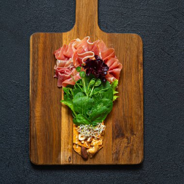 Jambon salatası (prosciutto) ıspanak ve marul, çıtır çıtır tuzlu ekmek, fındık, siyah arka planda mikroçerez. Gemide ampul şeklinde düz bir yiyecek yatağı var. Gıda enerjisi konsepti, üst görünüm.