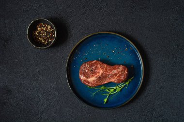 Çiğ mermer biftek, mikroyeşilliklerle pişirilmeye hazır. Bifteğin şekli ampuldür. İnsan için gıda enerjisi kavramı, üst görünüm, minimalizm.