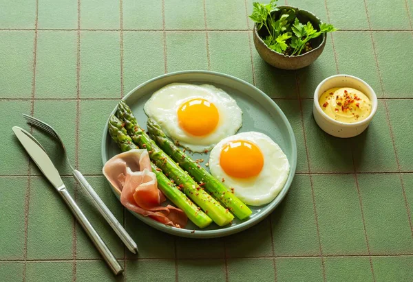 早餐煎蛋 新鲜芦笋和火腿 香草在一个绿色背景的盘子里 丰盛丰盛的早午餐 — 图库照片