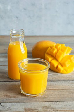 Bardakta taze mango suyu ve ahşap arka planda mango dilimi. Egzotik içecek, moda renkler.