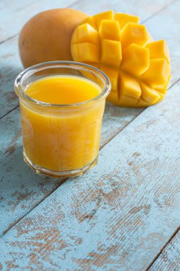 Bardakta taze mango suyu ve mavi ahşap arka planda mango dilimi. Egzotik içecek, moda renkler.