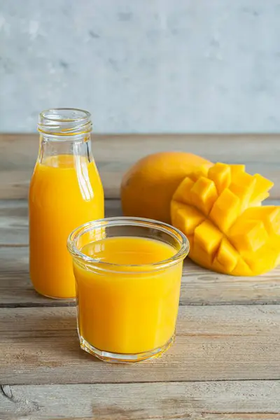 Fresh mango juice in a glass glass with mango slice on wooden background. Exotic drink, Trending colors.