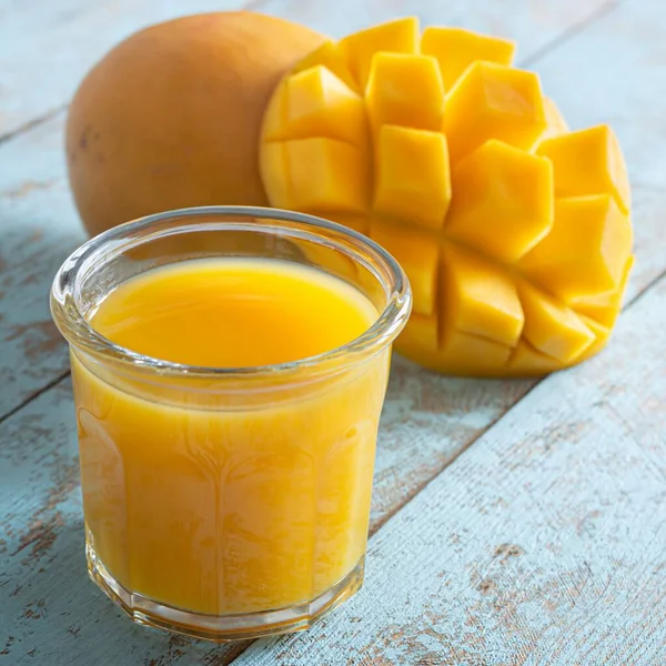 Bardakta taze mango suyu ve mavi ahşap arka planda mango dilimi. Egzotik içecek, moda renkler.