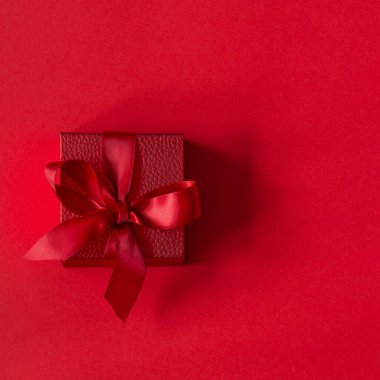 Kırmızı arkaplanda saten bir kurdele bulunan kırmızı bir hediye kutusu. Doğum günü, Noel, Sevgililer Günü, Anneler Günü konsepti.