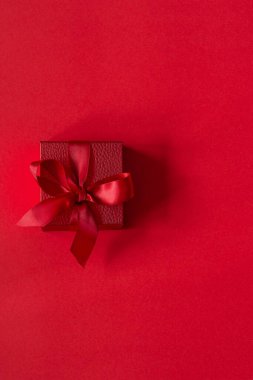 Kırmızı arkaplanda saten bir kurdele bulunan kırmızı bir hediye kutusu. Doğum günü, Noel, Sevgililer Günü, Anneler Günü konsepti.