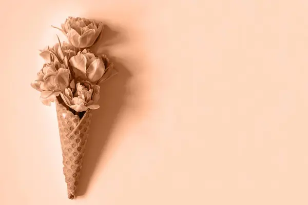 Şeftali arka planda laleli waffle (waffle) konisi. Çiçekli dondurma, ilkbahar konsepti ilk çiçeklerle, anneler günü, üst manzara. 2024 Yılının Rengi Şeftali Tüyleri.