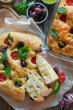 Fresh Italian flat bread Focaccia with tomatoes, olives, garlic and herbs on a wooden background.