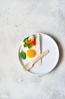 Healthy breakfast of fried egg and boiled vegetables with spinach on a light background. Healthy food concept, minimalism, top view.