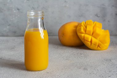 Gri arka planda mango dilimi olan taze mango suyu. Egzotik içecek, moda renkler.