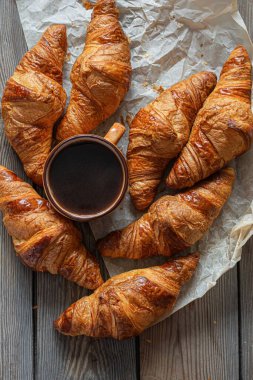 Ahşap zemin üzerinde bir fincan kapuçino (kahve) ile taze kruvasanlar. Popüler lezzetli kahvaltı..