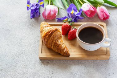 Happy mother's day, beautiful breakfast, lunch with cup of coffee (cappuccino) fresh croissants, strawberries on tray, bouquet of tulips as gift. Festive concept. Spring holiday, family relations.
