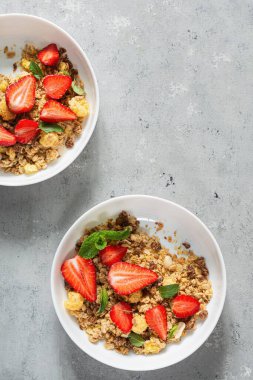 Beyaz bir tabakta fındıklı, kurutulmuş meyveli gevrek, taze çilek, nane ve yoğurt (mayalanmış süt). Sağlıklı kahvaltı kavramı.