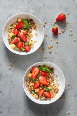 Beyaz bir tabakta fındıklı, kurutulmuş meyveli gevrek, taze çilek, nane ve yoğurt (mayalanmış süt). Sağlıklı kahvaltı kavramı.