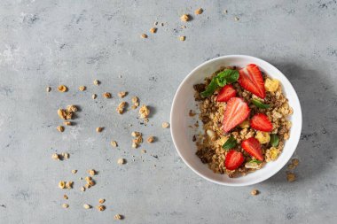 Beyaz bir tabakta fındıklı, kurutulmuş meyveli gevrek, taze çilek, nane ve yoğurt (mayalanmış süt). Sağlıklı kahvaltı kavramı.