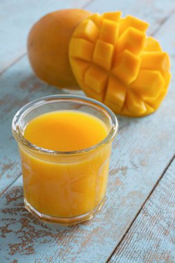 Mavi arka planda mango dilimli taze mango suyu. Egzotik içecek, moda renkler.