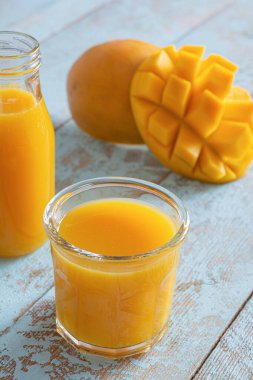 Bardakta taze mango suyu ve mavi ahşap arka planda mango dilimi. Egzotik içecek, moda renkler.