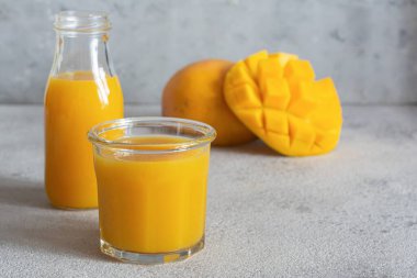 Gri arka planda mango dilimi olan taze mango suyu. Egzotik içecek, moda renkler.