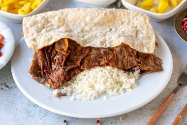 Gri arka planda pirinçli et donörü. Geleneksel tatlar. Biftek ve kuzudan yapılmış çörek kebabı. Kapat.