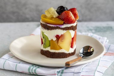 Gri arka planda meyveli kek. Çilekli, muzlu, kivili, şeftalili ve kremalı lezzetli bir pasta. Fırın ürünleri. Kapat.