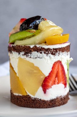 Gri arka planda meyveli kek. Çilekli, muzlu, kivili, şeftalili ve kremalı lezzetli bir pasta. Fırın ürünleri. Kapat.