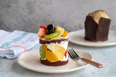 Gri arka planda meyveli kek. Çilekli, muzlu, kivili, şeftalili ve kremalı lezzetli bir pasta. Fırın ürünleri. Kapat.