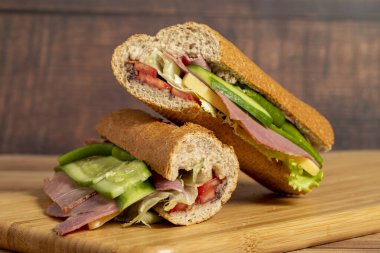 Ekmek arası sandviç. Salamlı sandviç, füme et, zeytin, marul, domates ve ahşap zemin üzerinde salatalık.