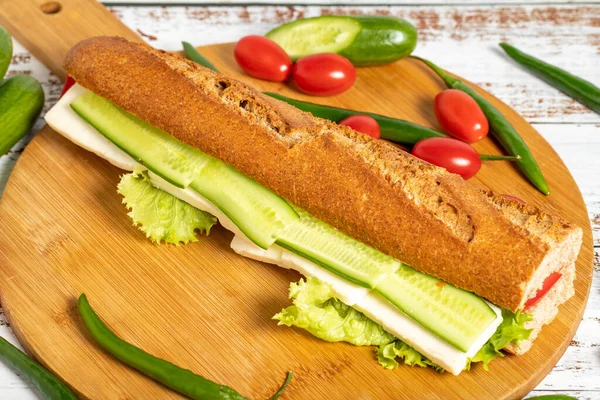 Baguette sandwich. Sandwich with olives, lettuce, tomato, cucumber, cheddar and feta cheese on wooden background