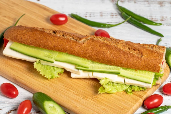 Baguette sandwich. Sandwich with olives, lettuce, tomato, cucumber, cheddar and feta cheese on wooden background