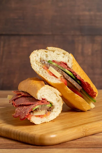 Baguette sandwich. Sandwich with salami, roast beef, cheddar, tomato and cucumber on wooden background