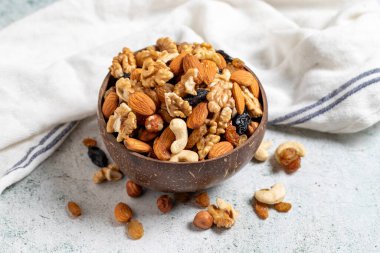 Gri arka planda çiğ fındık. Hindistan cevizi kasesinde ceviz, badem, fındık ve kuru üzüm. Kapat.